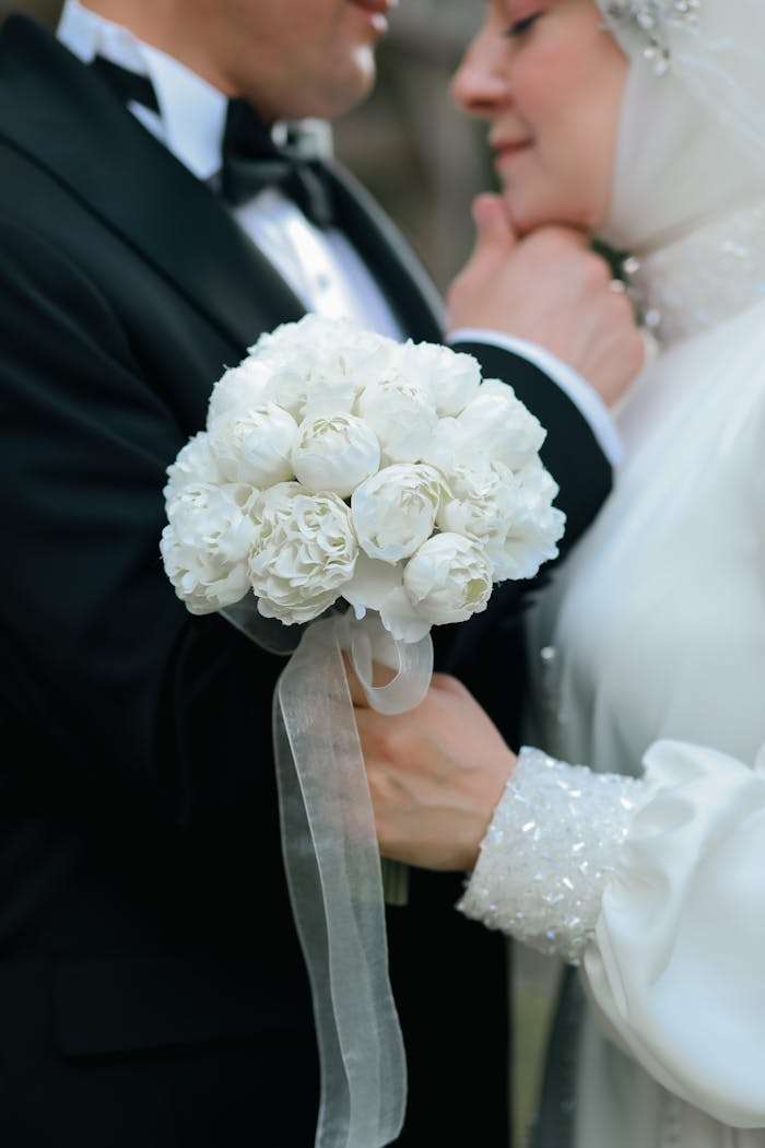 services-03 Close-up of a newlywed couple holding a white flower bouquet, capturing their intimate moment.